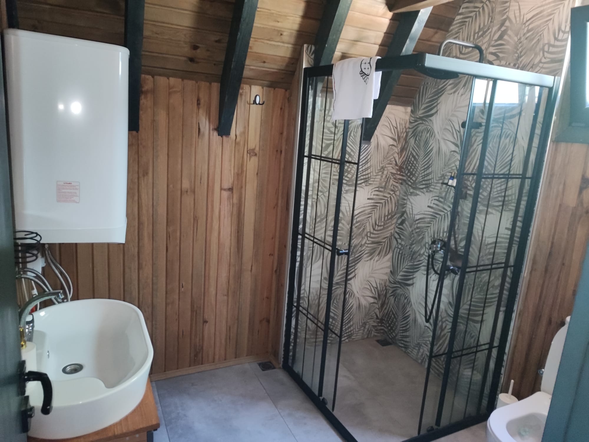 Wood-panelled en-suite bathroom with a glass walk-in shower over palm-leaf tiling and a white vessel sink.