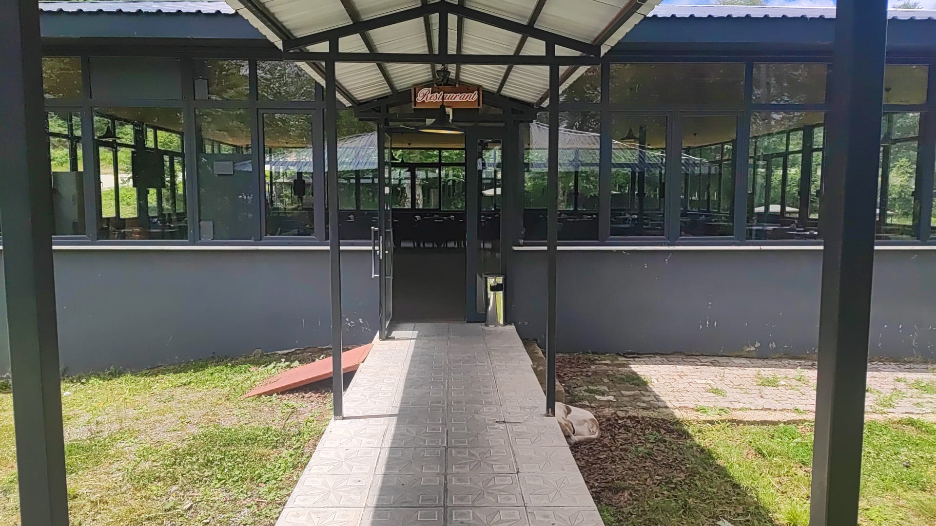 The covered glass entry walkway to the restaurant, with the Restaurant sign over the door and a tiled path leading in.