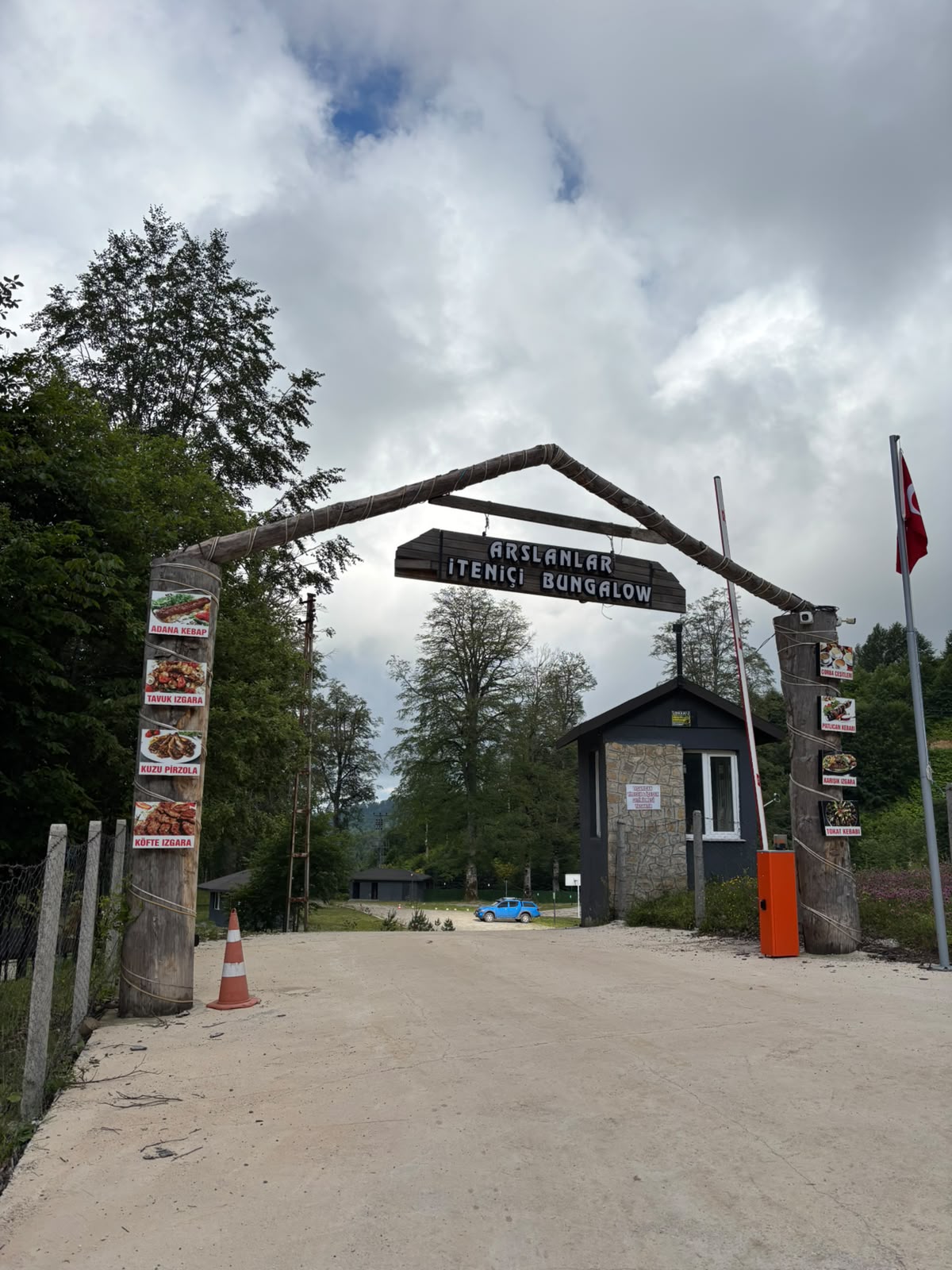 The timber entrance arch reading Arslanlar İteniçi Bungalow, with a stone gatehouse, barrier and Turkish flag at the forest road.